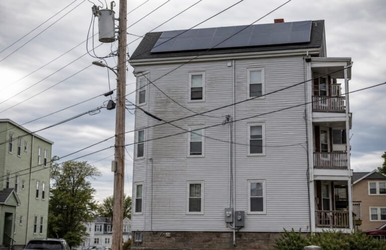Massachusetts utility pole transformer beside a triple-decker with rooftop solar, illustrating Simplified interconnection upgrade costs.