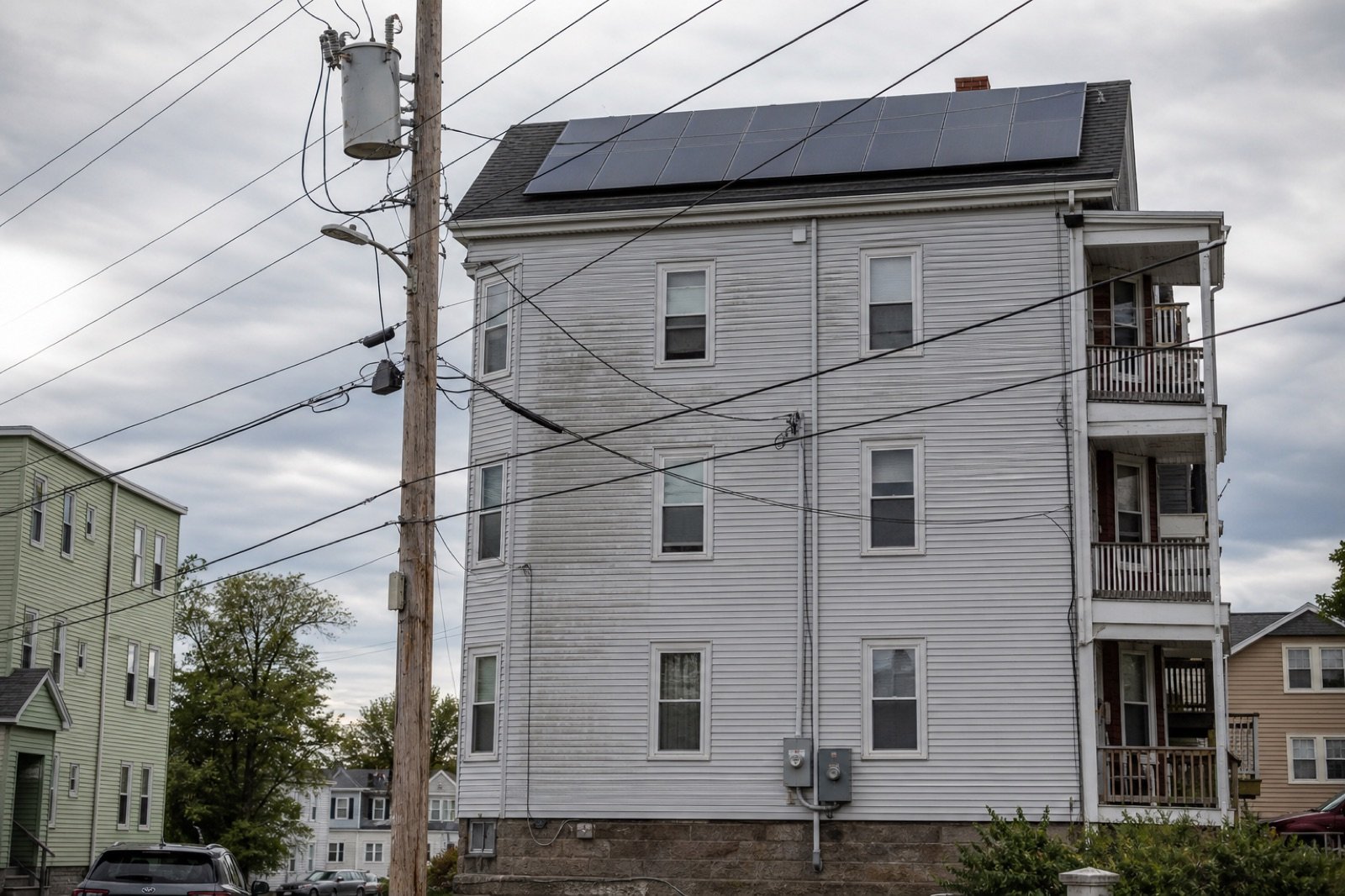 Massachusetts utility pole transformer beside a triple-decker with rooftop solar, illustrating Simplified interconnection upgrade costs.