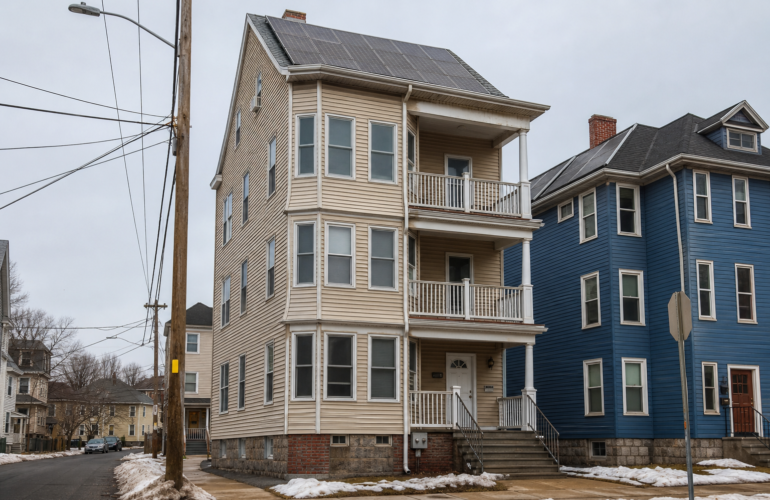 Worcester Massachusetts triple-decker with rooftop solar under a gray sky.