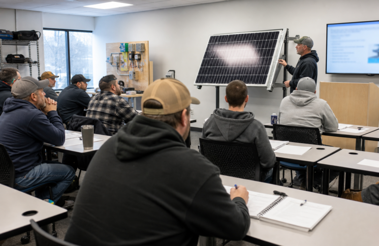 Solar training classroom with a PV module on a stand and installers taking notes.